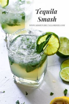 two glasses filled with ice and limes next to some sliced lemons on a white surface