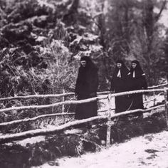 an old photo of three women standing by a fence in the snow, with trees behind them