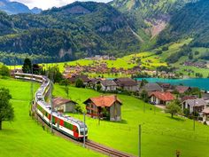 a train traveling through a lush green countryside next to houses and mountains in the background