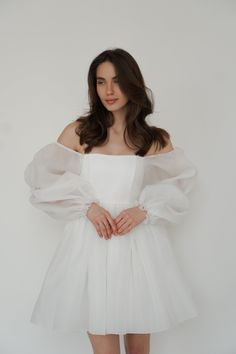 a woman in a white dress posing with her hands on her hips and looking at the camera