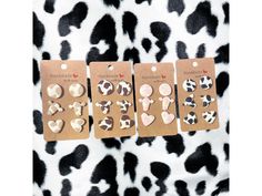 four pairs of animal print earrings are shown in front of a black and white spotted background