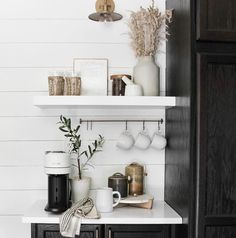 a kitchen with black cabinets and white walls, coffee mugs on the shelf above