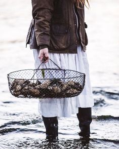 a woman standing in the water holding a basket full of oysters