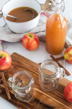 an apple cider, cinnamon sticks and apples on a cutting board next to two jars