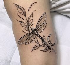 a black and white photo of a dragonfly tattoo on the leg, with leaves around it