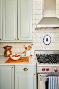 a kitchen with green cabinets and white tile backsplash, stainless steel range hood