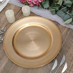 a gold plate with beaded edges sits on a wooden table next to silverware and flowers