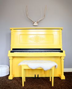 a yellow piano with the words we paint pianos on it and a deer head mounted to the wall