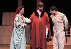 two men and a woman dressed in medieval clothing standing on stage talking to each other