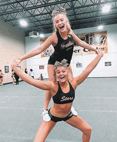 two cheerleaders in black and gold outfits are posing for the camera with their hands up