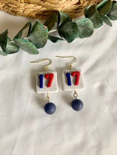 two pairs of earrings with red, white and blue letters on them next to a basket