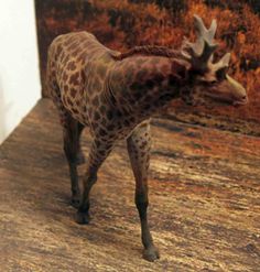 a giraffe standing on top of a wooden floor next to a white wall