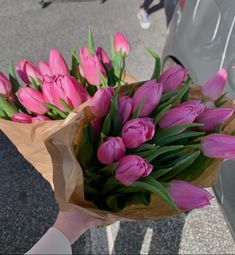 a person holding a bouquet of pink tulips in front of a parked car