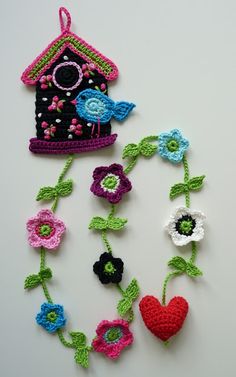 crocheted birdhouse and flower garland on white surface with red heart in center