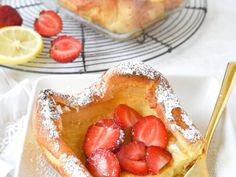 a heart shaped pastry with powdered sugar and sliced strawberries on the plate next to it