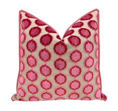 a pink and white pillow with red circles on the front, sitting on a white surface