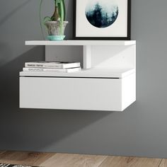 a white shelf with some books and a vase on it next to a gray wall