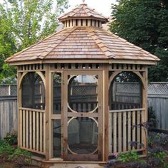 a wooden gazebo sitting in the middle of a garden next to a fence and trees