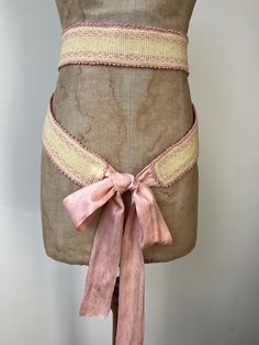 A very pretty 19th century sash belt. The body appears to be crocheted cream cotton finished with dainty scalloped edging and embroidered with cross stitch. Lined with pink cotton. At each end, there are long, luxurious silk ribbon ties in pretty sugar pink.  Highly wearable and lovely to display.  Measurements: The body alone- 140 x 6cm Each silk ribbon- 74 x 6cm.  Condition: The silk has scatters of fox marks throughout. The body has some minor darkening and two tea-coloured marks next to one Belt Ribbon, Silk Crochet, Embroidered Corset Belt, Adjustable Embroidered Brown Belt, Adjustable Brown Embroidered Belt, Crochet Belt Inspire Uplift ⭐, Roses Au Crochet, Embroidered Belt, Sash Belts