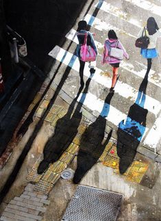 three people walking down the street with their shadows on the ground and one person holding an umbrella