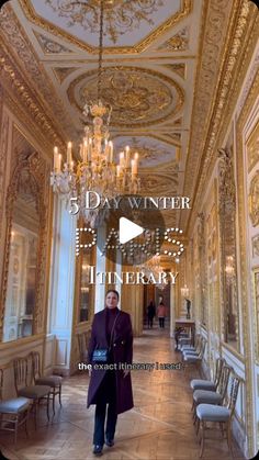 a man in a purple coat walking down a hall with chandeliers and chairs