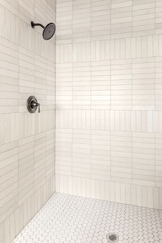 a white tiled shower with thermostaer and hand held shower head in it