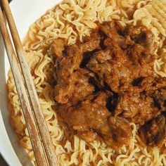 a white plate topped with meat and noodles next to chopsticks on a table