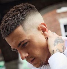 a close up of a person with a shaved head and tattoos on his arm, wearing a white shirt