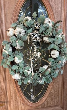 a skeleton wreath with green leaves and white pumpkins is hanging on the front door