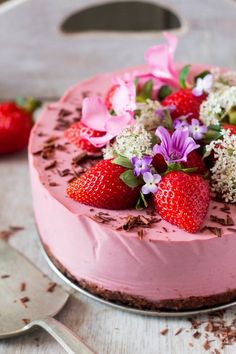 a cake with pink frosting and strawberries on top, next to two forks