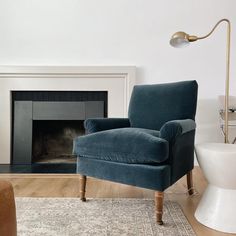 a blue chair sitting in front of a fire place next to a white wall and wooden floor