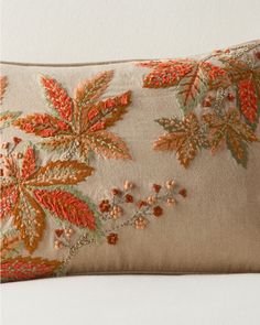 an embroidered pillow with orange and green leaves on it's side, sitting on a white couch