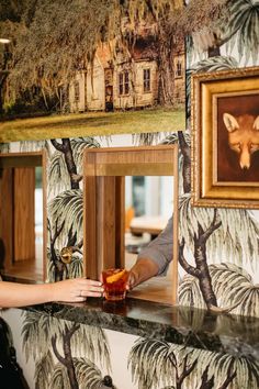 a woman is reaching for a drink in front of a wall with pictures on it