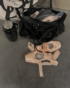 an open black bag sitting on the ground next to ballet shoes