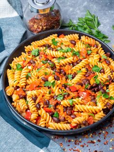 a skillet filled with pasta and beans on top of a blue towel next to some parsley