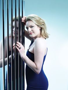 a woman in a blue dress leaning against a metal wall