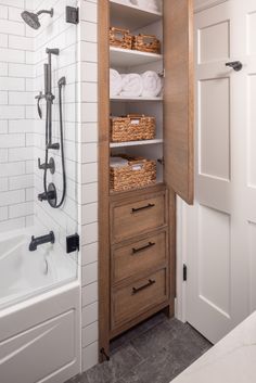 an open cabinet in the bathroom with towels and baskets on it's shelves next to a bathtub