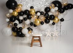 black, white and gold balloons are hanging in the background with a stool underneath them