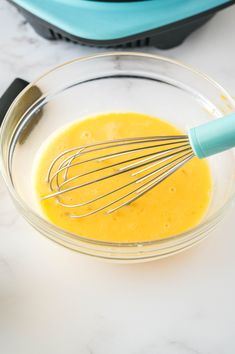 a glass bowl filled with yellow liquid and whisk on top of a counter