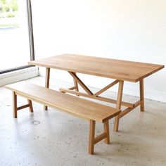 a wooden table and bench sitting in front of a window with no one around it