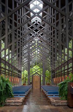 the inside of a church with blue pews and plants on either side of it