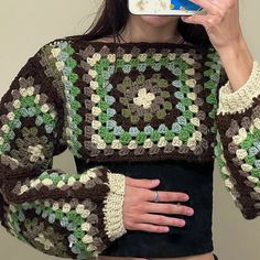 a woman taking a selfie with her cell phone wearing a crocheted sweater