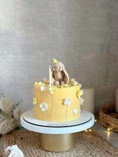 there is a yellow cake with white flowers and a teddy bear sitting on the top