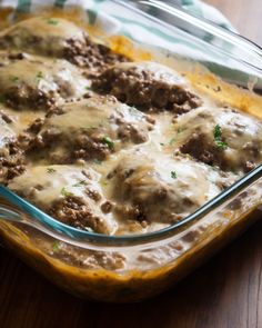 a casserole dish filled with meat and gravy on top of a wooden table