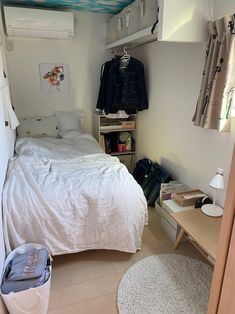 a bedroom with a bed, desk and clothes hanging on the wall