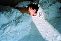 a woman laying in bed with her head on the pillow and white sheets covering it