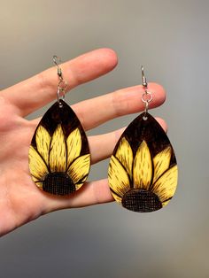 a pair of yellow and black earrings on a person's hand, with the image of a sunflower painted on it