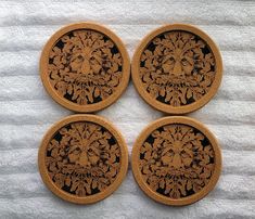 four wooden coasters with designs on them sitting on a white cloth covered tablecloth