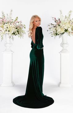 a woman in a long green dress standing next to two white vases with flowers