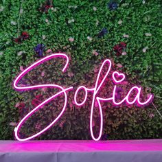 a neon sign that says sofia in front of a green wall with flowers